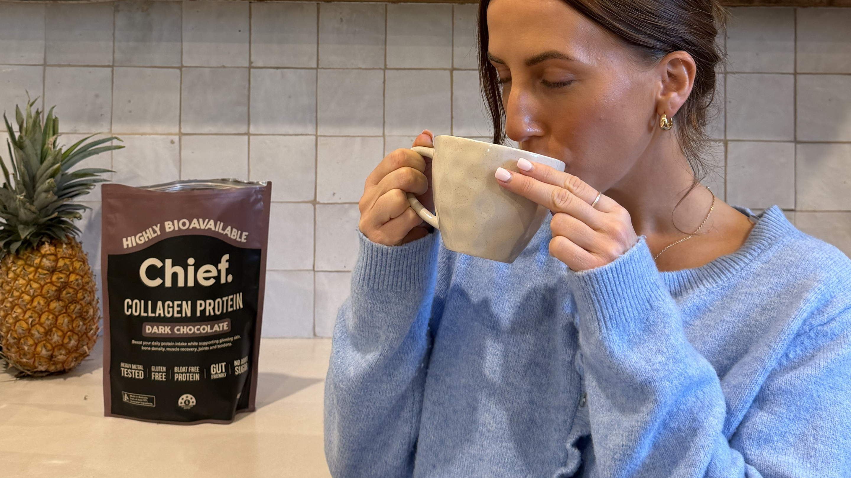 Image is of a women drinking coffee with Dark Chocolate Chief Collagen powder mixed in